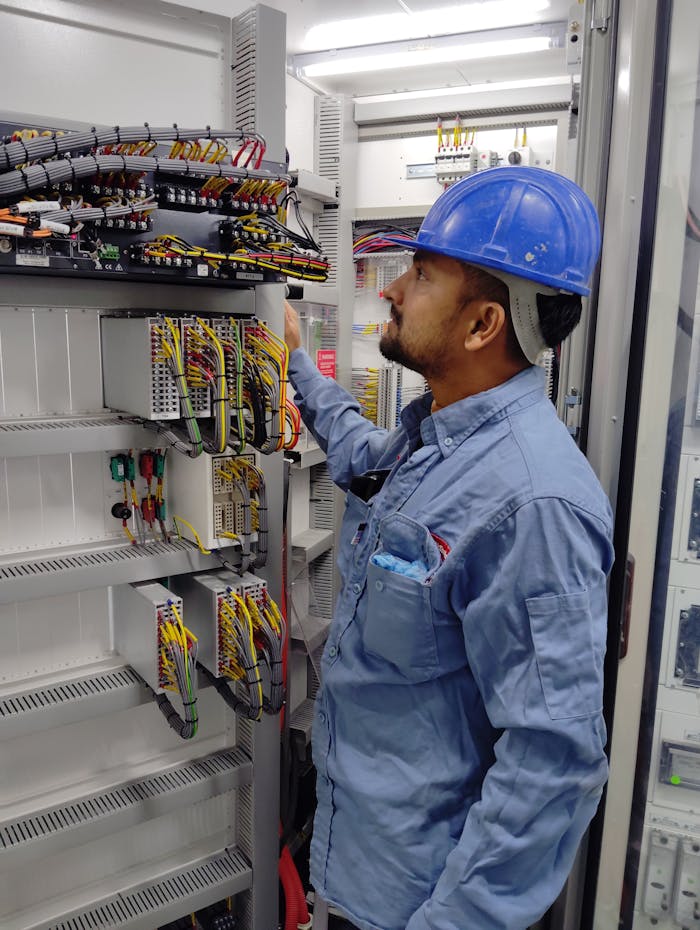 gallery-6 Electrician in blue helmet checking control panel wiring for safety compliance.