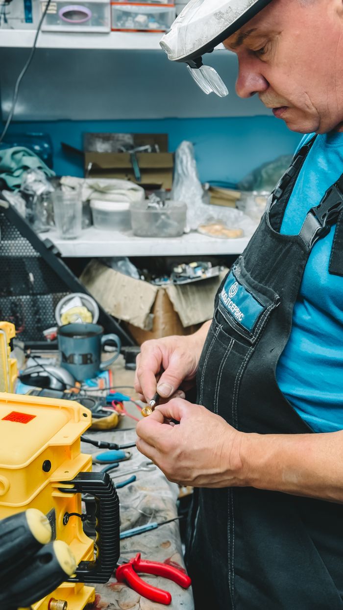 services-01 A technician repairs machinery parts in a busy workshop, showcasing precision and detail.