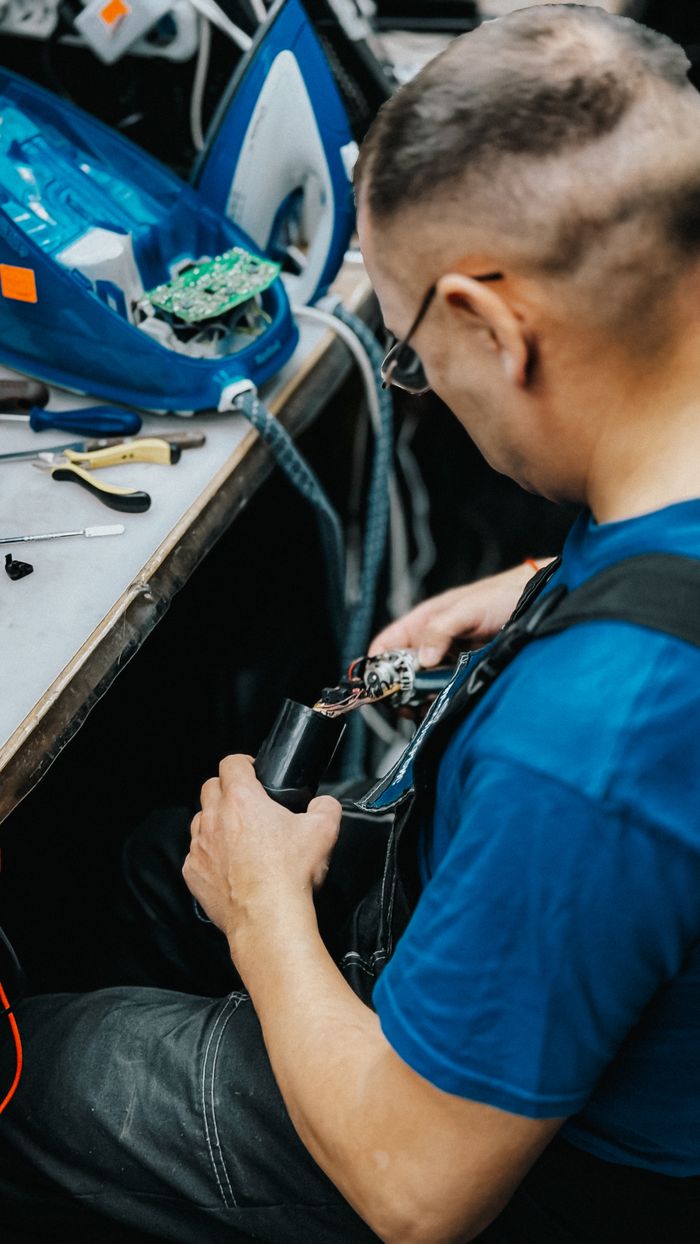 about-01 A skilled technician repairs an electronic device indoors, focused on intricate wiring and components.