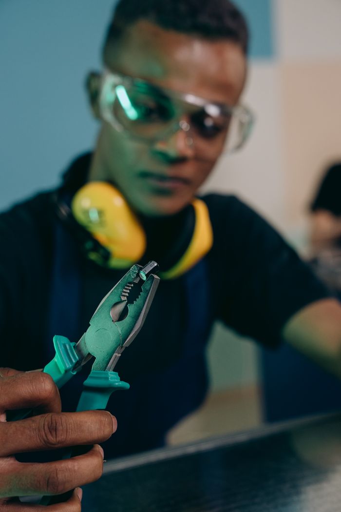 Focused worker holding pliers and wearing safety gear in an indoor setting.
